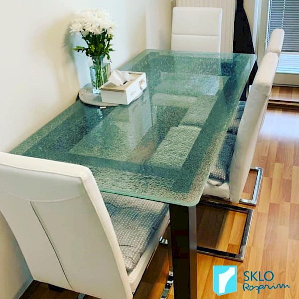 Skleněný jídelní stů- ve vzhledu crash glass s černými nohami a čtyřmi bílými židlemi