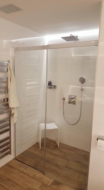 Skleněná zástěna oddělující prostor sprchový kout se stoličkou od zbytku koupelny