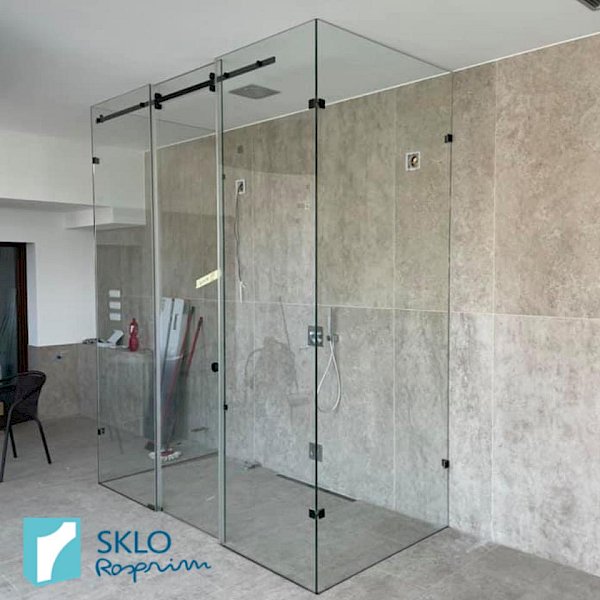 Skleněné zástěny sprchového koutu v prostorné koupelně s velkými běžovo-šedými dlaždicemi