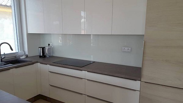 Skleněná deska do kuchyně za kuchyňskou linkou v kuchyni s bílými skříňkami se dřevěnými prvky