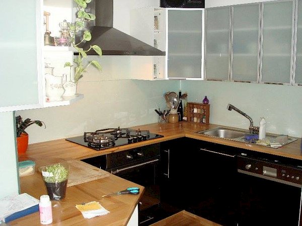 Kuchyně se skleněnou deskou za kuchyňskou linkou a skleněnými dvířky horních skříněk