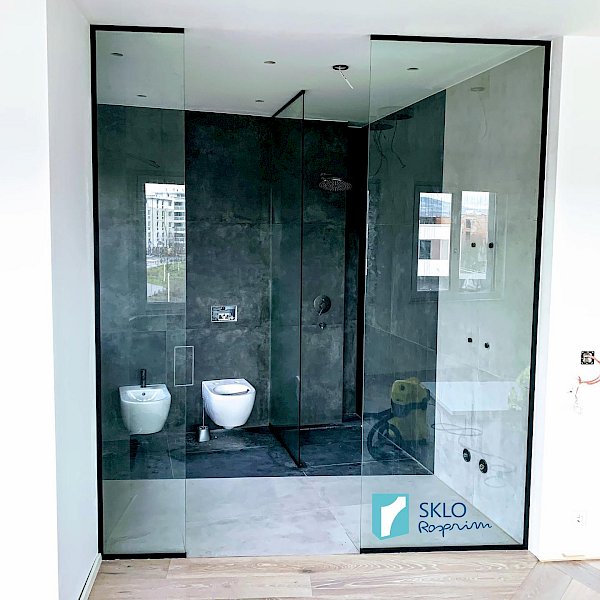 Skleněné zástěny s černým orámováním v koupelně, průhled do koupelny v kombinaci bílých a šedých dlaždic