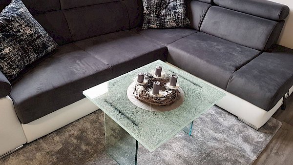 Šedá pohovka a skleněný konferenční stolek s horní deskou crashglass